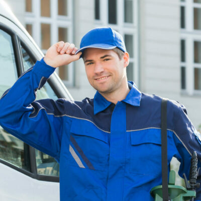 Portrait of happy pest control worker wearing cap while standing against truck